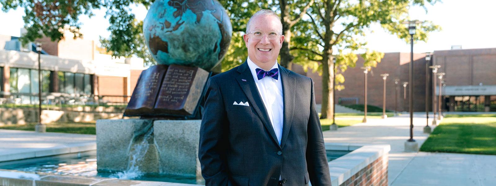 President Melson smiling while standing in front of globe water sculpture